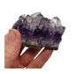 A hand holding a piece of amethyst with purple points on a base of grey stone