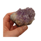 A hand holding a piece of amethyst with purple points on a base of grey stone