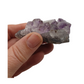 A hand holding a piece of amethyst with purple points on a base of grey stone