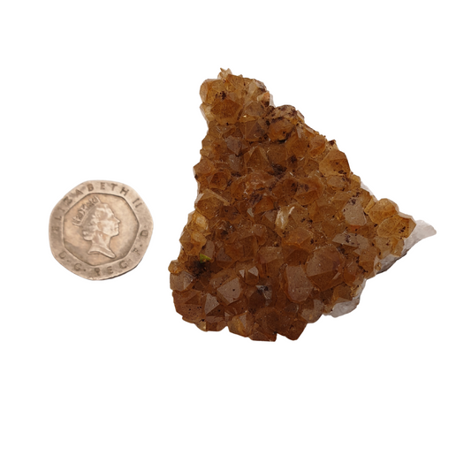 A cluster of citrine with yellow crystal points on a white base next to a 20 pence 