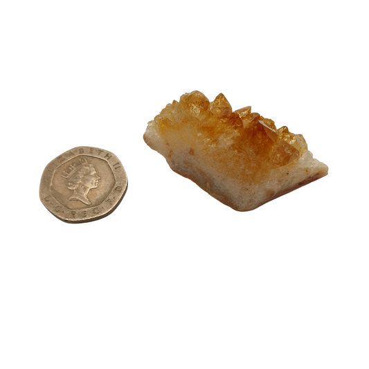 A cluster of citrine with yellow crystal points on a white base next to a 20 pence 