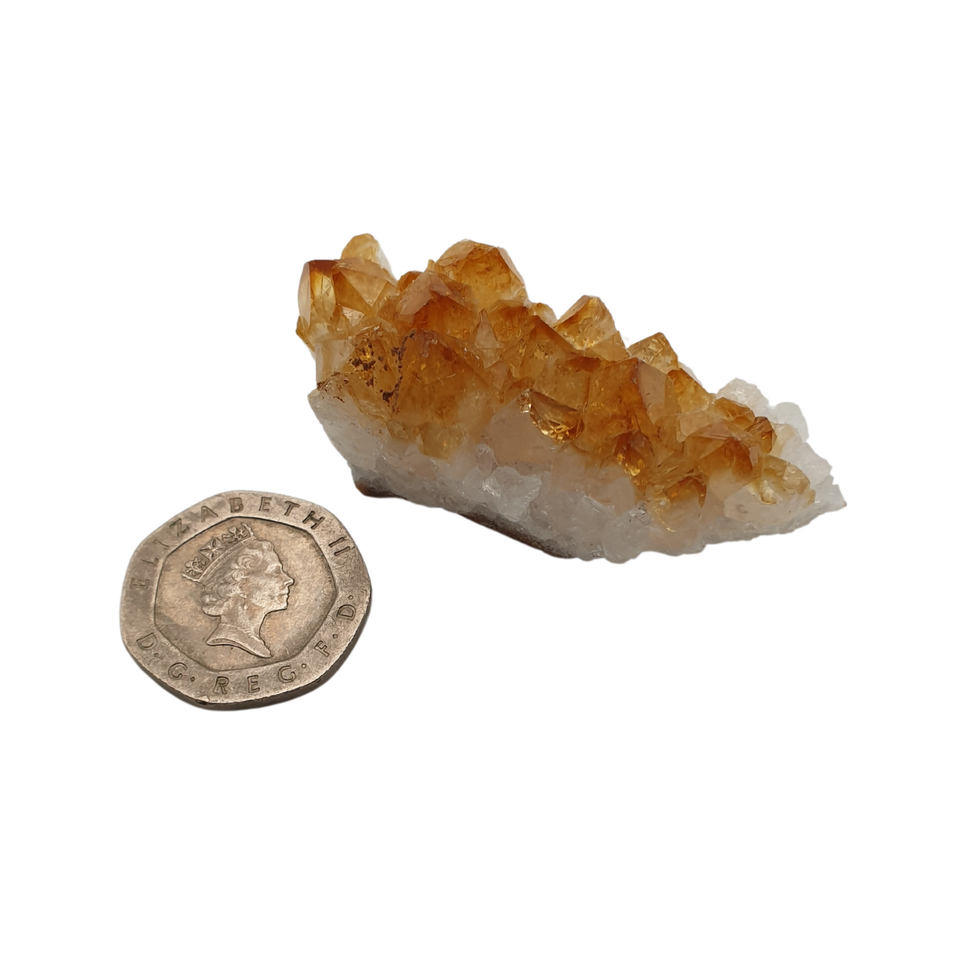 A cluster of citrine with yellow crystal points on a white base next to a 20 pence 