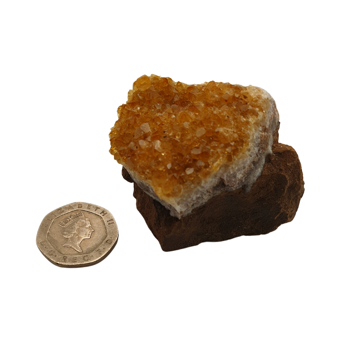 A cluster of citrine with yellow crystal points on a white base next to a 20 pence 