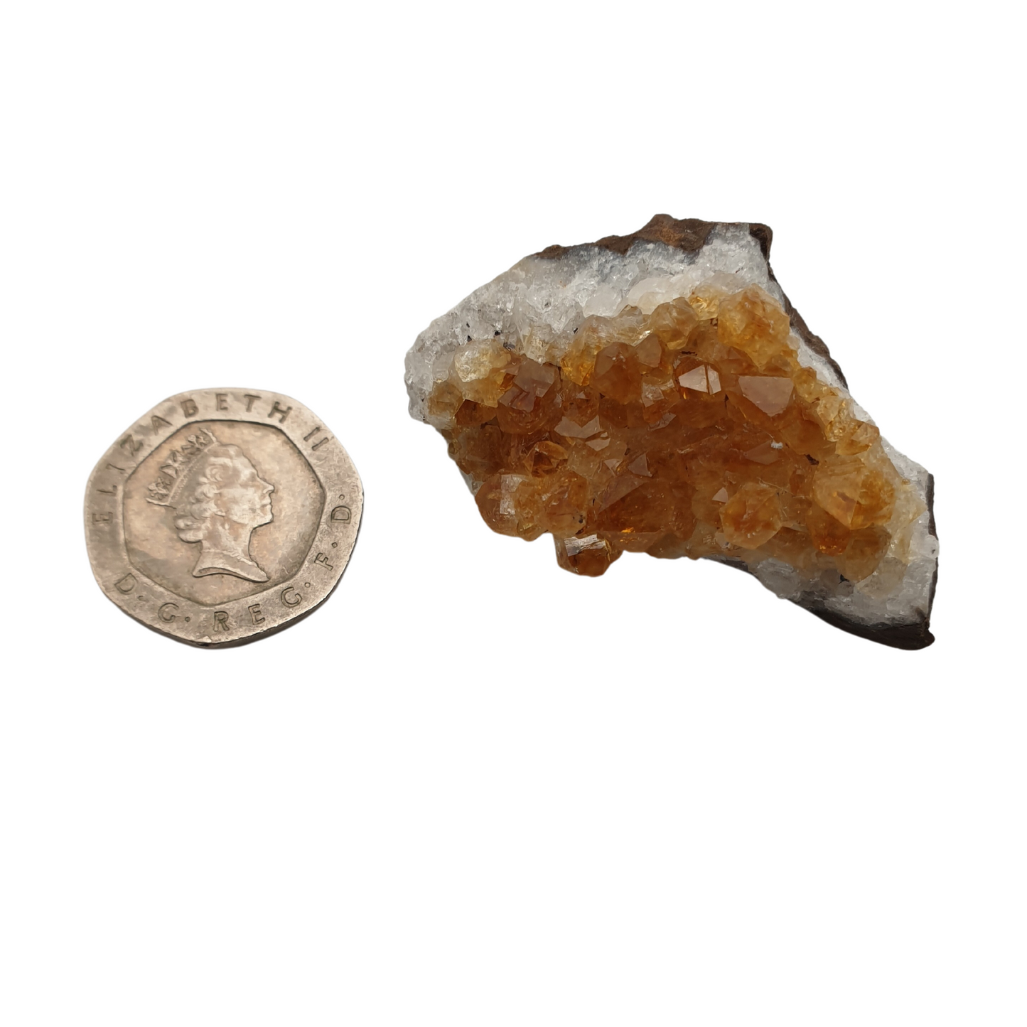 A cluster of citrine with yellow crystal points on a white base next to a 20 pence 