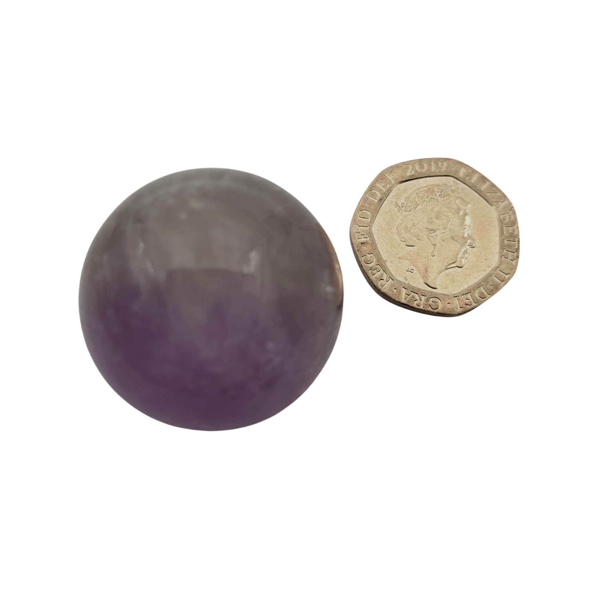 An amethyst carved into a sphere next to a 20 pence piece on a white background