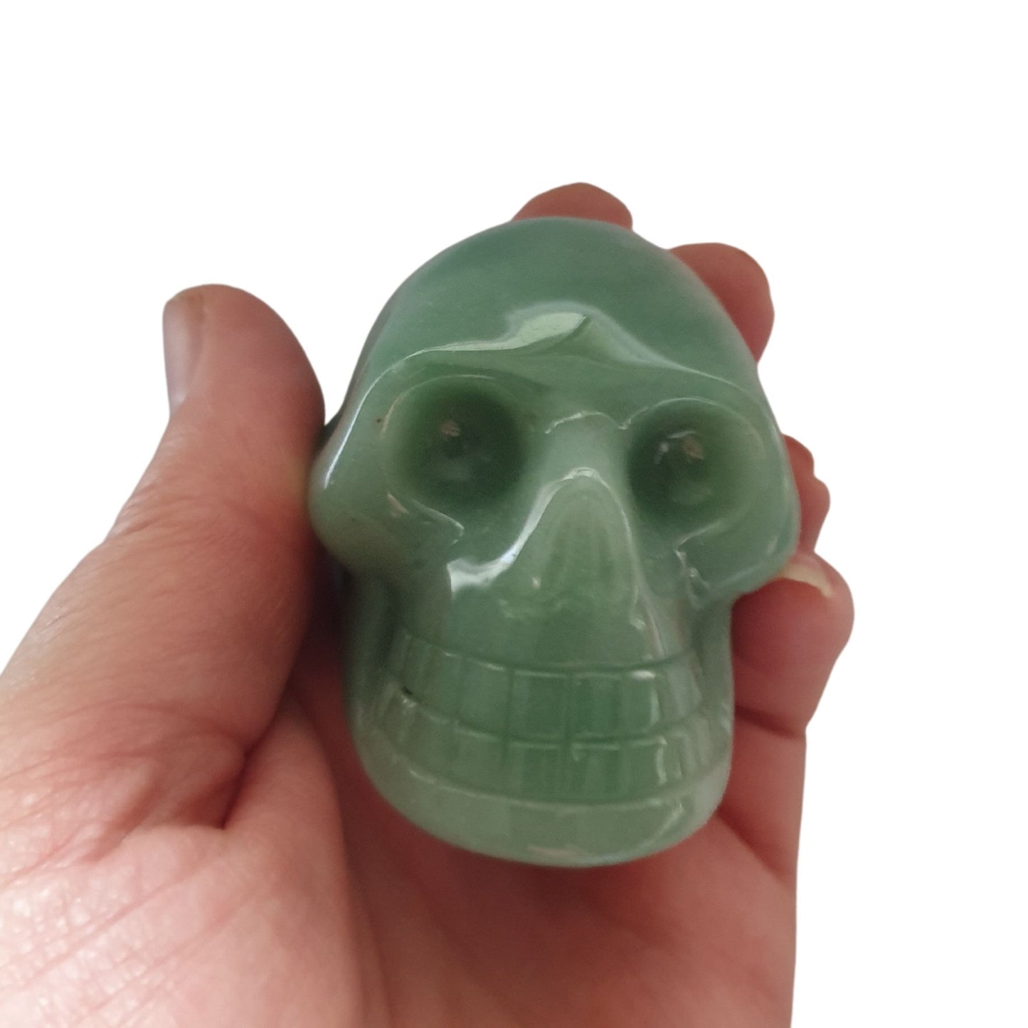 A hand holding a skull carved from green aventurine crystal